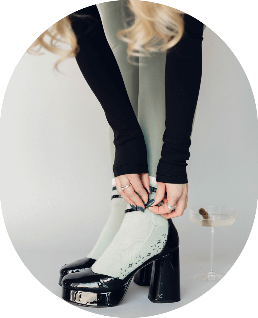 Girl fastening her high heels over her grippy Pilates socks that match a dirty martini behind her.