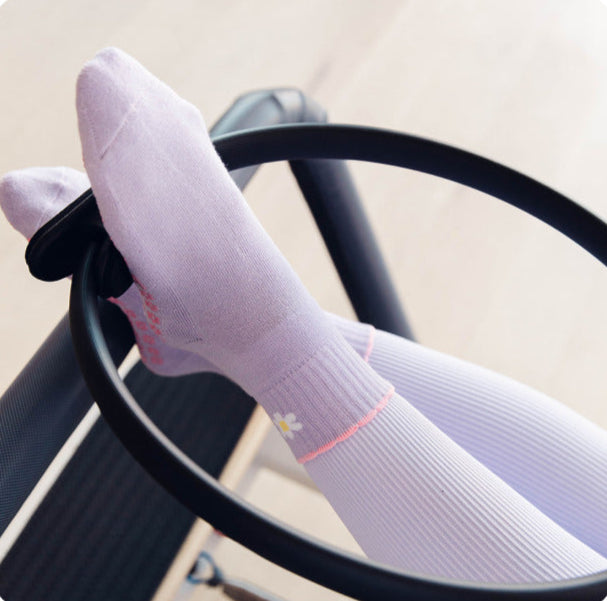Lilac daisy Pilates sock with matching purple leggings doing Pilates exercises.